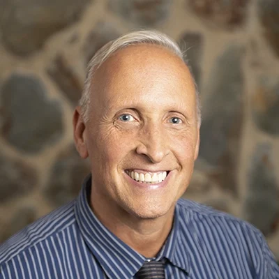 Chiropractor Jason Finch Smiling In Front Of Cobble Wall