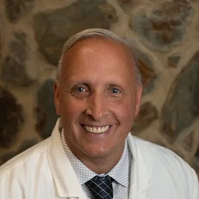 Chiropractor Jason Finch Smiling In Front Of Cobble Wall