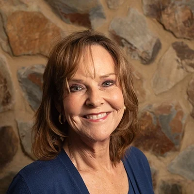 Chiropractor Marianne Taylor Bauman Smiling In Front Of Cobble Wall